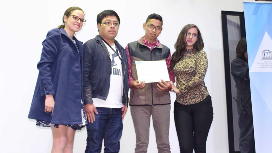 María Brown (UNESCO-Quito) entrega la mención de honor a Danilo Bohorquez, Adrián Carrión y Belén García, estudiantes de la UPS
